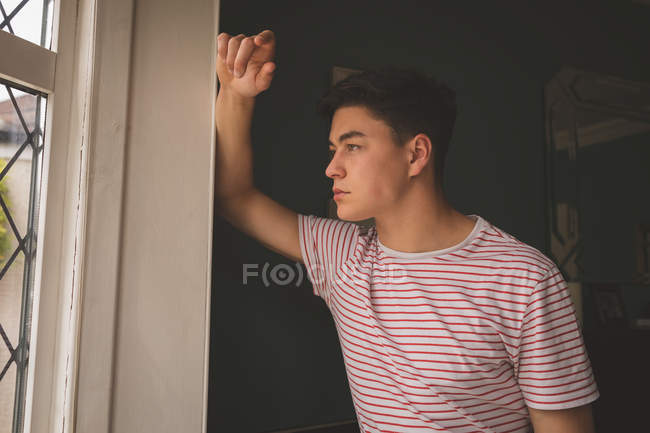Man leaning on wall and looking through window at home. — Stock Photo