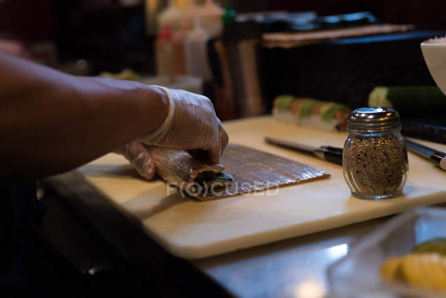 Chef rodando sushi desenrollado sobre tabla de cortar - foto de stock