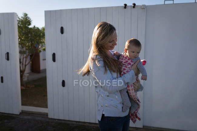Mother holding baby while standing in backyard in sunlight. — Stock Photo