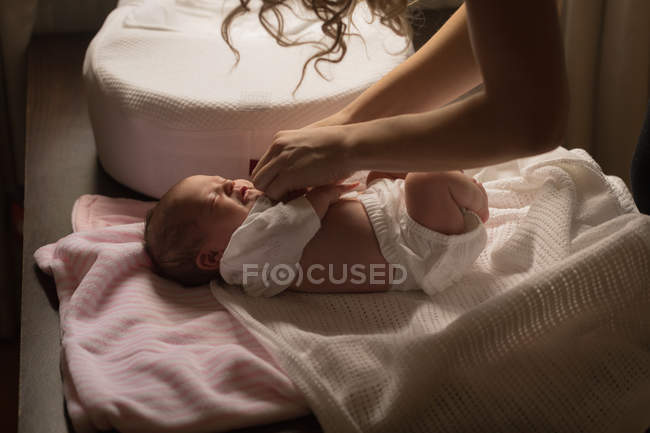 Mother dressing newborn baby girl at bed. — Stock Photo
