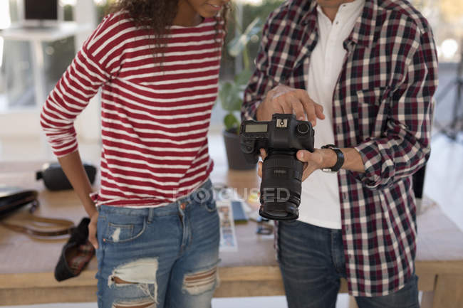 Mid section of photographer showing photos to fashion model on digital camera in studio — Stock Photo