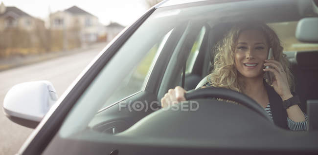 Усміхнена жінка-виконавця розмовляє на мобільному телефоні під час водіння автомобіля — стокове фото