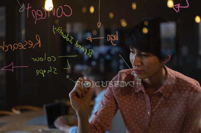 Exécutif féminin écrivant des notes sur le mur de verre au bureau . — Photo de stock