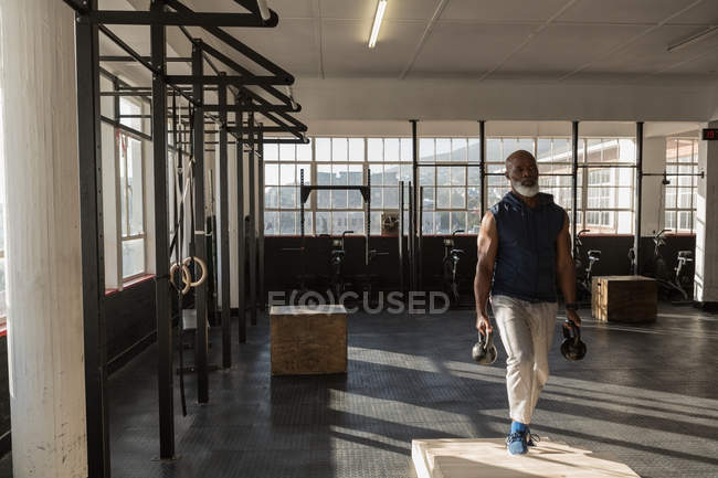 Homem sênior determinado exercitando com kettlebells no estúdio de fitness . — Fotografia de Stock