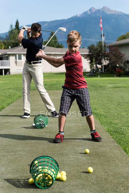 Padre e hijo golpeando tiro de golf en el campo - foto de stock