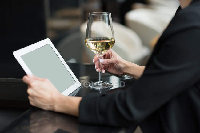 Sezione centrale della donna d'affari utilizzando un tablet digitale e tenendo in mano un bicchiere di champagne — Foto stock