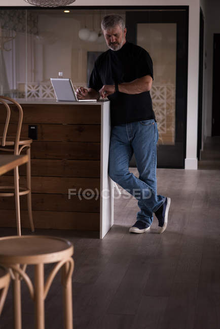 Männlicher Büroleiter überprüft die Uhrzeit auf der Smartwatch, während er im Kreativbüro Laptop benutzt — Stockfoto