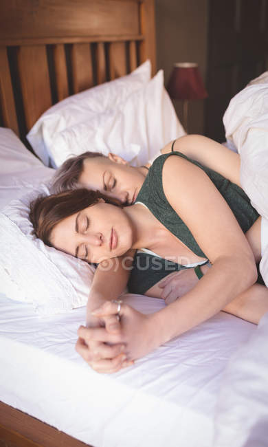 Лесбійську пару, тримаючись за руки під час сну на ліжку в спальні в домашніх умовах. — стокове фото