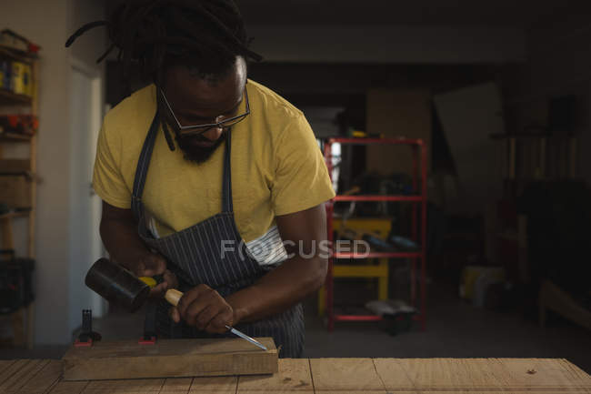Carpenter carving wood at table in workshop — Stock Photo