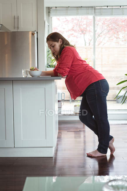 Pregnant woman looking at her mobile phone while having breakfast at home — Stock Photo