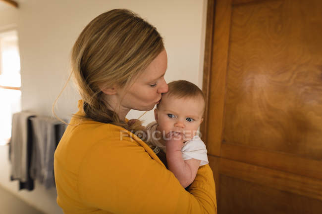 Мать носит и целует маленького сына дома . — стоковое фото