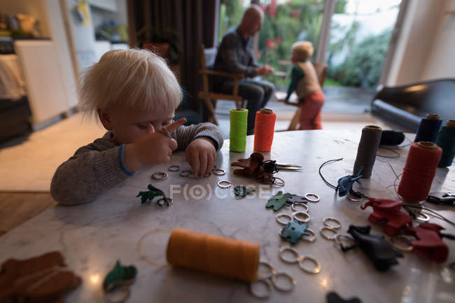 Niña jugando con hilos de coser con la familia en el fondo en casa . - foto de stock