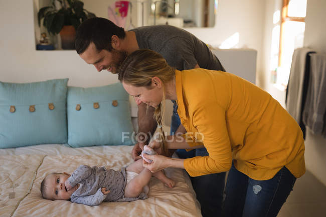 Parents changing diaper of baby son on bed at home. — Stock Photo