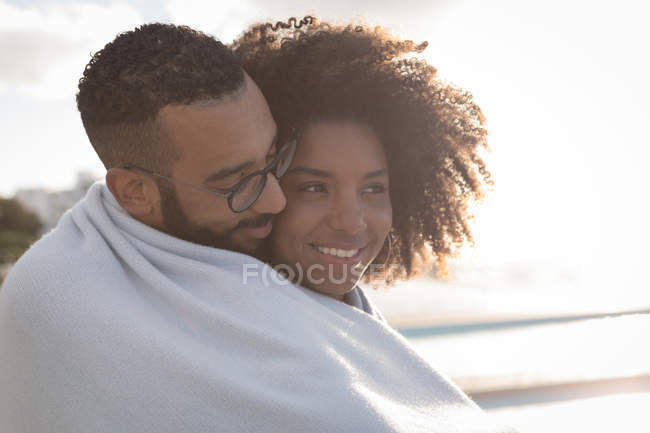 Coppia romantica avvolta nello scialle vicino a una spiaggia in una giornata di sole — Foto stock