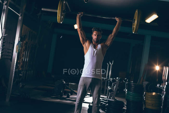 Retrato de un hombre musculoso haciendo ejercicio con barra en el gimnasio - foto de stock