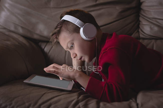 Хлопчик використовує цифровий планшет з навушниками у вітальні вдома — стокове фото