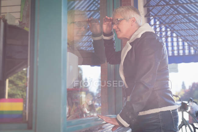 Donna anziana sbirciare attraverso la finestra di vetro fuori dalla libreria — Foto stock