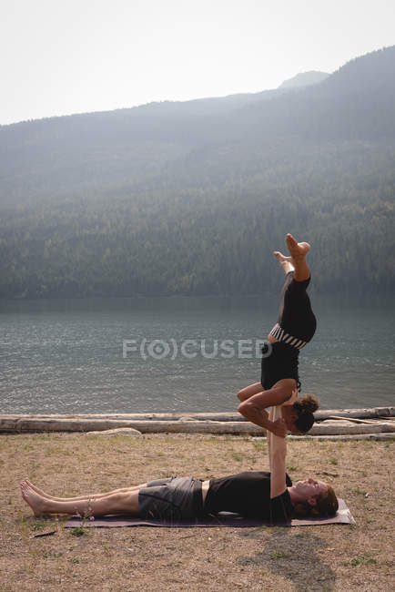 Pareja deportiva practicando acro yoga cerca de la costa del mar en un día soleado - foto de stock