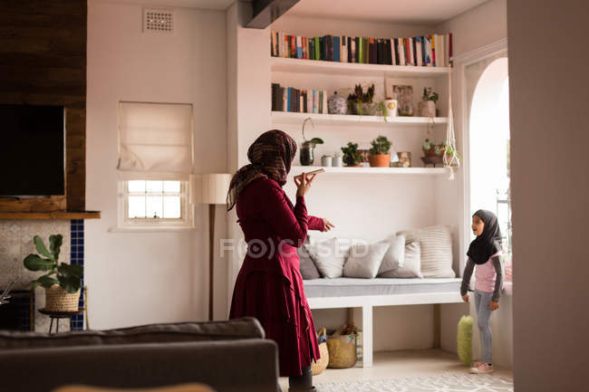 Mulher muçulmana conversando com sua filha enquanto usa o telefone em casa — Fotografia de Stock