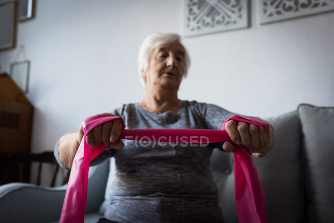 Donna anziana che esegue esercizio con banda di resistenza in soggiorno a casa — Foto stock
