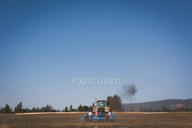 Трактор вспахивает поле в солнечный день — стоковое фото