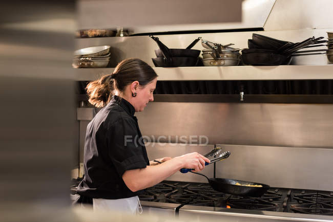 Chef mezclando la verdura en la sartén mientras cocina en la cocina comercial - foto de stock