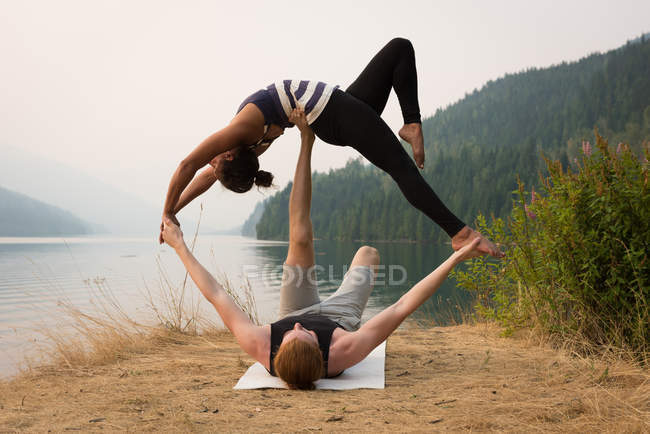 Pareja en forma practicando acro yoga en un exuberante terreno verde a la hora del amanecer - foto de stock