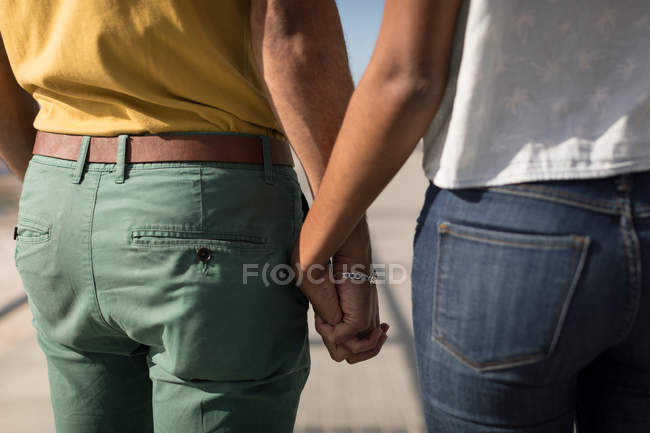 Sección media de la pareja cogida de la mano en un día soleado - foto de stock