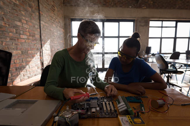 Mother teaching daughter about soldering iron in office. — Stock Photo
