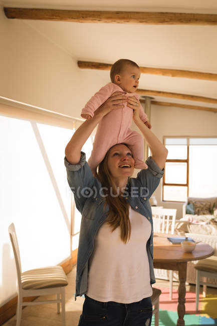 Feliz madre jugando y levantando bebé hijo en casa - foto de stock
