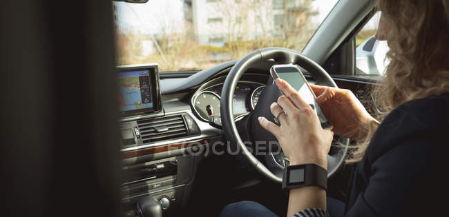 Vue latérale de l'exécutif féminin en utilisant mobile dans la voiture — Photo de stock