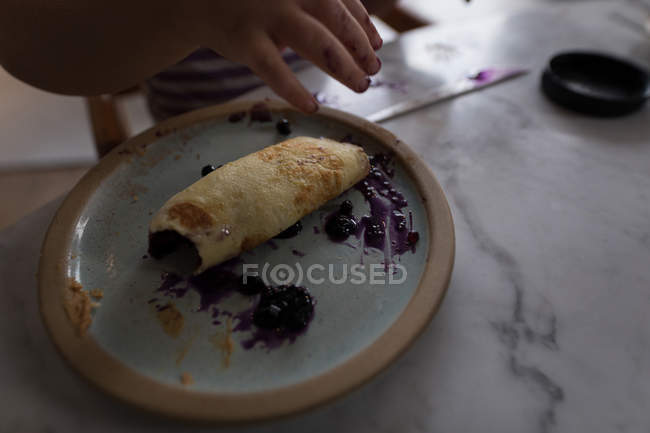Close-up of toddler hands eating jam roll at home. — Stock Photo