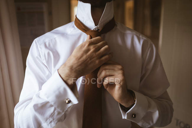 Sección media del hombre usando la corbata en casa - foto de stock