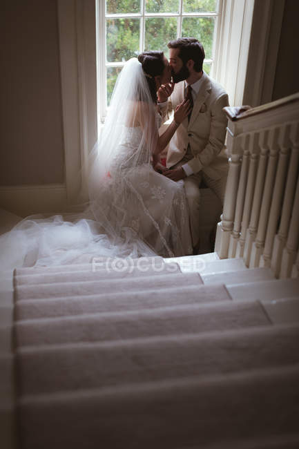 Romantic bride and groom sitting on the window sill and kissing — Stock Photo