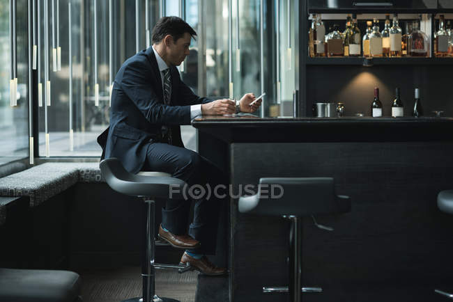 Businessman using mobile phone while having whiskey at hotel counter — Stock Photo