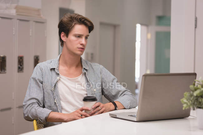 Ejecutivo usando el ordenador portátil mientras toma café en la oficina creativa - foto de stock