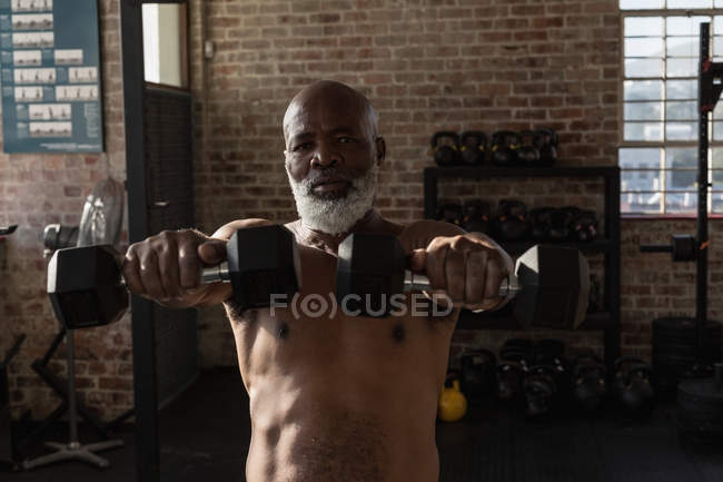 Решительный старший мужчина упражняется с гантелями в фитнес-студии . — стоковое фото