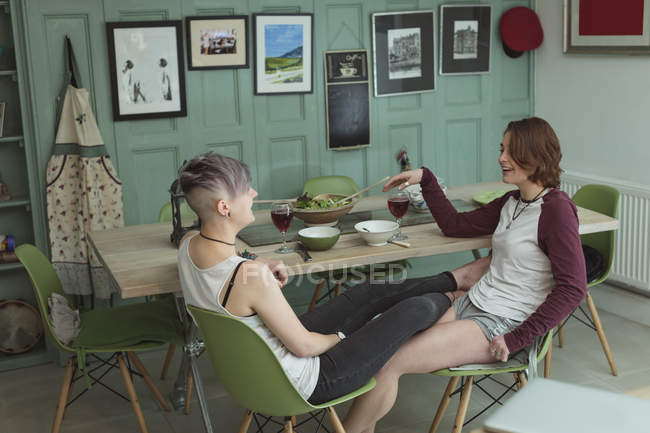 Pareja lesbiana cenando con copas de vino tinto en la moderna sala de estar . - foto de stock