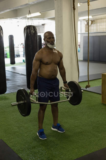 Determined senior man exercising with barbell in fitness studio. — Stock Photo