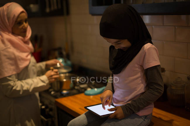 Muslim mother cooking while daughter using digital tablet in kitchen — Stock Photo