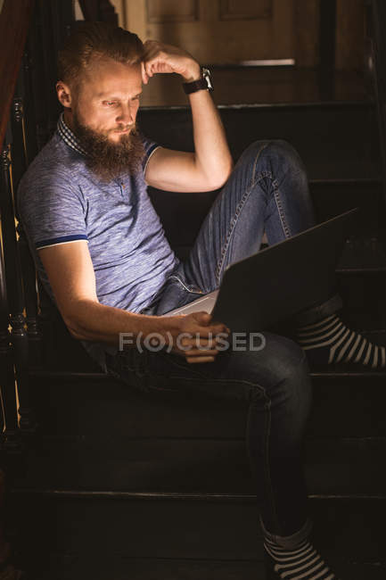 Gros plan d'un homme utilisant son ordinateur portable assis sur un escalier à la maison — Photo de stock