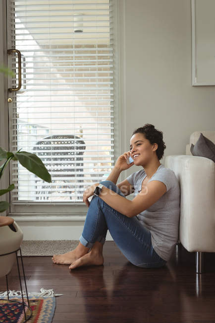 Donna felice che parla sul cellulare vicino al divano a casa — Foto stock