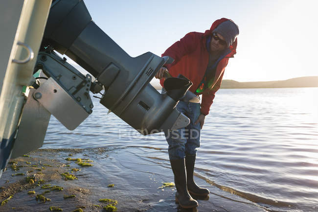 Homem verificando barco a motor perto do lado do rio à luz do sol . — Fotografia de Stock