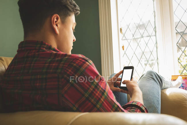 Homem usando telefone celular na sala de estar por janela . — Fotografia de Stock