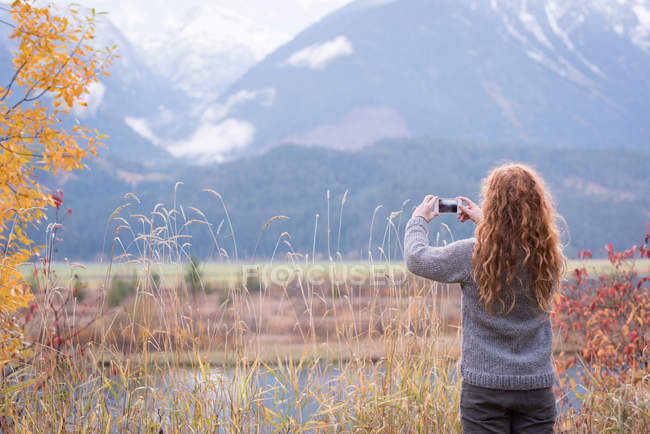 Vue arrière de la femme prenant une photo de montagne avec téléphone portable — Photo de stock