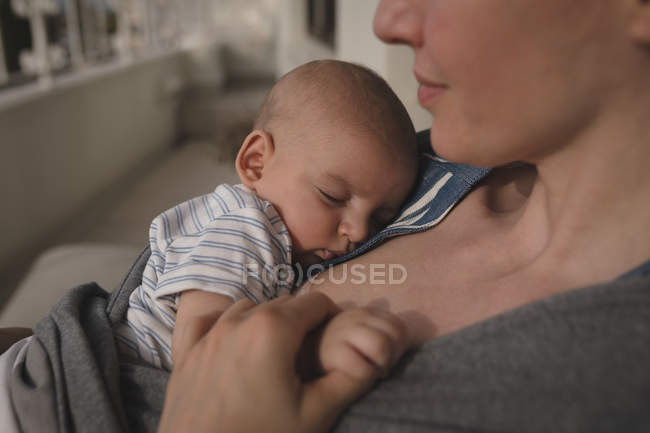 Primer plano de mamá joven sosteniendo al bebé dormido en casa - foto de stock