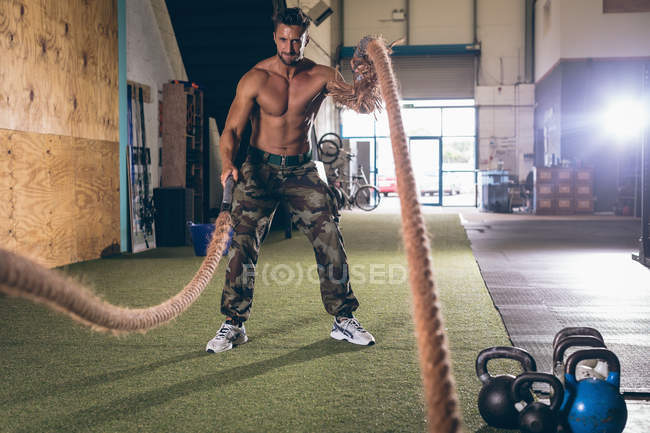 Hombre musculoso determinado haciendo ejercicio con cuerda en el gimnasio - foto de stock
