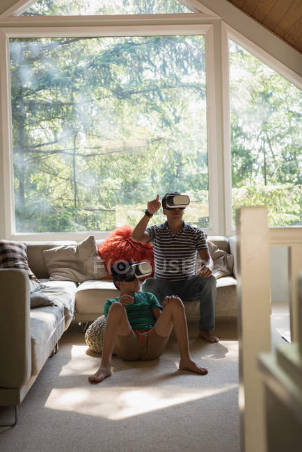 Padre e hijo usando auriculares de realidad virtual en la sala de estar en casa - foto de stock