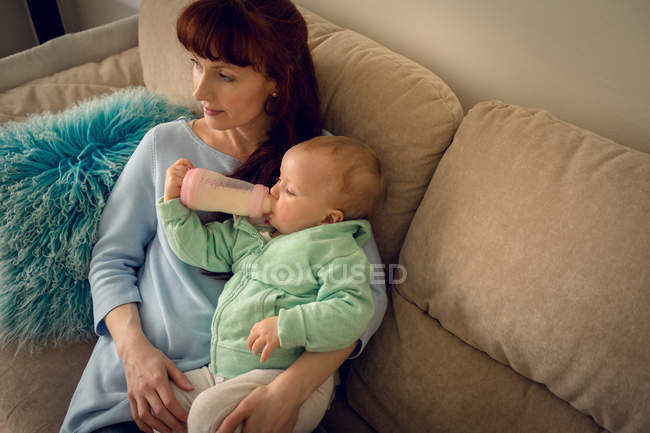 Baby girl with his mother drinking milk from baby bottle at home — Stock Photo