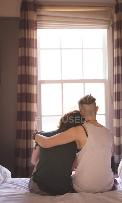 Rückansicht von lesbischem Paar, das im Schlafzimmer auf dem Bett sitzt und sich zu Hause umarmt. — Stockfoto